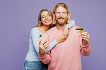 Young happy couple two friends family man woman wear pink blue casual clothes together using mobile cell phone hold credit bank card shopping online order delivery isolated on plain purple background.