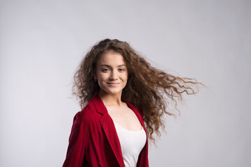 Portrait of a gorgeous teenage girl with curly hair in red blazer. Studio shot, white background...