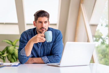 Thinking man sitting at desk with his laptop and working from home