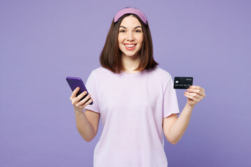 Young happy calm woman wear pyjamas jam sleep eye mask rest relax at home using mobile cell phone credit bank card shopping online order delivery isolated on plain purple background Night nap concept