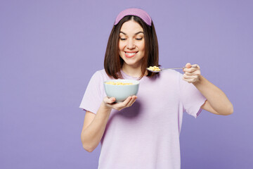 Young calm woman wear pyjamas jam sleep eye mask rest relax at home eat breakfast muesli cereals...