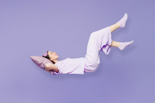 Full body side view young fun calm woman she wear pyjamas jam sleep eye mask rest relax at home fly up hover over air fall down isolated on plain pastel purple background. Good mood night nap concept.