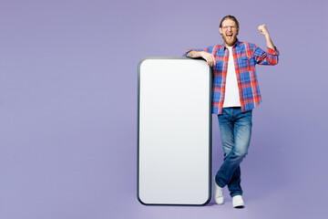 Full body young happy man wear blue shirt casual clothes big huge blank screen mobile cell phone smartphone with area do winner gesture isolated on plain pastel purple background. Lifestyle concept