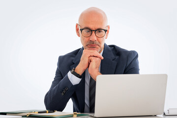 Mid aged businessman sitting at desk and using notebook for work against isolated background