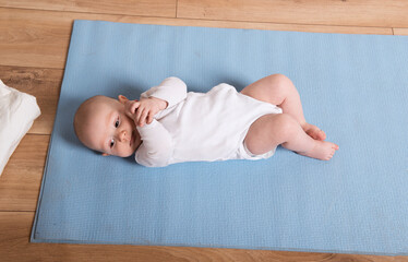 Portrait of an adorable baby lying on a mat on the floor, looking at the camera and smiling.