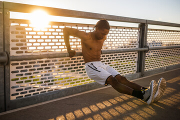 Young african-american man is exercising on the bridge in the city. He is doing reverse push-ups.