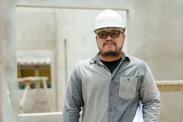 Builder with a safety helmet standing confidently at a construction site. Engineer with hard hat and blueprints, overseeing construction work.