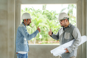 Male construction professionals in helmets give thumbs up, signaling success in building project. Work of construction engineers on the job site