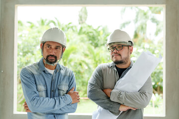 Confident construction workers in hard hats stand with arms crossed, blueprint in hand, project...