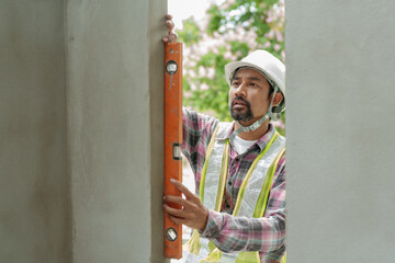Focused male construction worker in helmet uses spirit level on wall, professional, precise in...