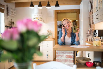 Beautiful mature woman at home, phone calling and drinking hot herbal tea. Older woman living alone, enjoying peaceful weekend day