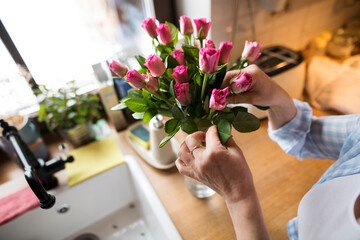 Beautiful mature woman arranging bouquet of roses in a vase, a hobby and relaxation. Older woman...