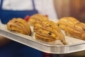 Baker carrying freshly baked crispy golden cakes on a metal tray to cool