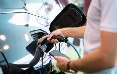 Male person charging his electric car. Closeup charger in hand.