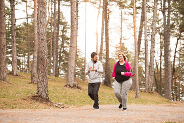 An overweight woman running in nature with friend. Exercising outdoors for people with obesity, support from friend, fitness coach.