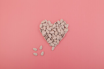 Pills or Multivitamins in heart shapes on pink background. Healthy supplements. Vitamins B, C, D,...