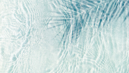 transparent rippled water surface with palm leaf shadow at the sand beach on a summer day, abstract idyllic beach vacation background from above with copy space