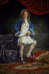 Medieval person, senior man posing wearing old-fashioned clothes posing with sword against vintage...
