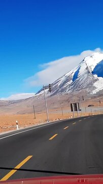 The POV perspective shows a car traveling on the G314 national highway in the Pamir Plateau of Kachin Prefecture, Xinjiang, along the Mushtag Peak section of the Karakoram Highway.