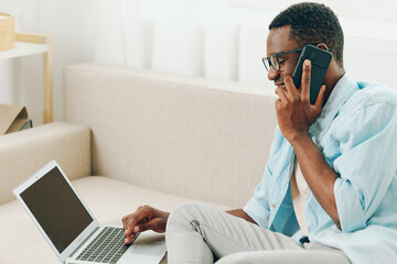Smiling African American Man Working on Laptop and Making Online Shopping Call in Home Office The...
