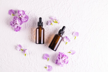 Top view of cosmetic bottles made of dark glass with a pipette with a natural facial skin care product. . Flat lay. White background, flowers.