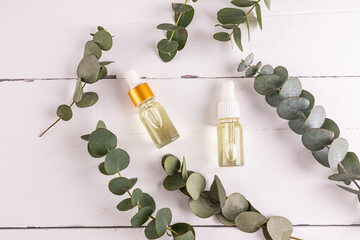 Two light glass cosmetic bottles with natural eucalyptus oil for facial skin care. rejuvenation, cell regeneration. top view. eucalyptus branches.