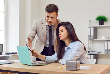 Business male executive manager mentor giving consultation to female colleague using laptop sitting in office desk, investment advisor at work, startup project, discussing ideas, pointing at monitor