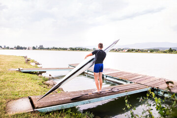 Young canoeist carry canoe and paddle, going into water, walking on wooden dock. Concept of...
