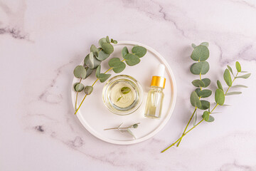 Natural cosmetic eucalyptus oil in a bowl and cosmetic bottle on an tray among eucalyptus twigs. Top view. Natural cosmetics. Marble Background.