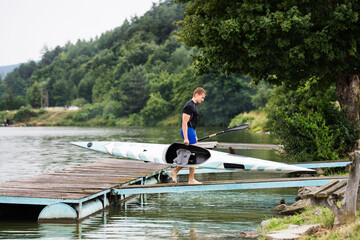 Young canoeist carry canoe and paddle, going into water, walking on wooden dock. Concept of...
