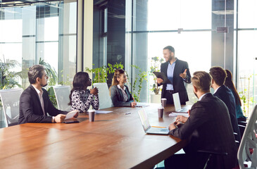 Diverse joyful confident people sitting at big table in meeting room having business conference in...