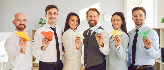 Portrait of happy smiling business people with paper planes in hands standing in office in a row...