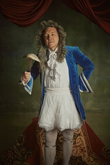 Portrait of elderly man dressed in richly detailed baroque costume posing holding fish on fork...
