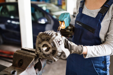 Female auto mechanic repairing, maintaining car. Beautiful woman working in a garage, wearing blue...