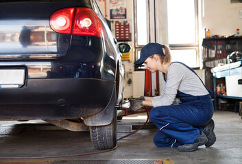 Female auto mechanic changing tieres in auto service. Beautiful woman holding tire in a garage,...