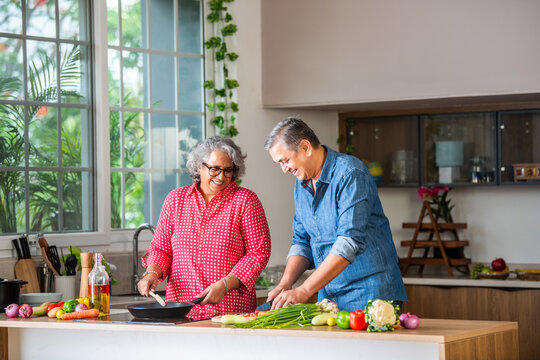 Senior Indian asian couple in kitchen, cooking healthy food together and happy in retirement lifestyle.