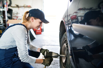 Female auto mechanic changing tieres in auto service. Beautiful woman kneeling by wheel in a...