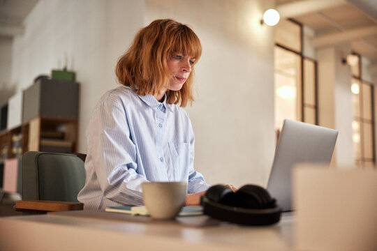 Businesswoman with red hair and casual work clothes, working at her office desk in an open office community