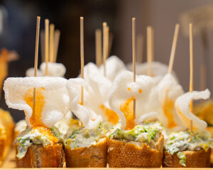 Typical snack of Basque Country, pinchos or pinxtos skewers with small pieces of bread, sea food, eggs, cheese served in bar in Bilbao, Spain, close up.