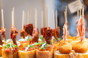 Typical snack of Basque Country, pinchos or pinxtos skewers with small pieces of bread, cheese, sundried tomato and jamon served in bar in  Bilbao, Spain, close up. Selective focus. Soft focus.