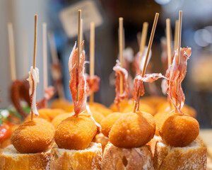 Typical snack of Basque Country, pinchos or pinxtos skewers with small pieces of bread, cheese, jamon served in bar. Basque pinchos (a form of Spanish tapas), with bread and Spanish ham, in a bar.