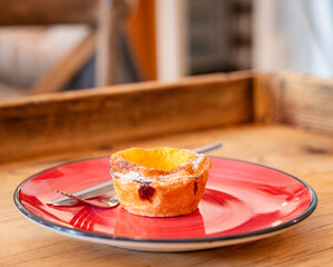 Traditional pastel de nata custard tart on a red plate with a knife and fork. One Pastel de nata or Portuguese egg tart. Small pie with a crispy puff pastry crust and a custard cream filling.