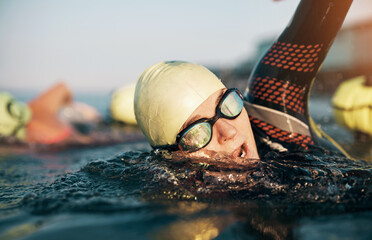 Mature woman and her class doing an open ocean swim together. She wears a wetsuit and swimming goggles while swimming front crawl.