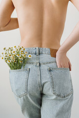 Backside view of young pretty woman with naked top. Chamomile flowers bouquet in jeans pocket