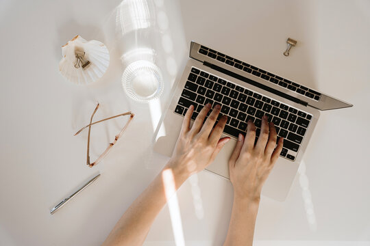 Closeup view of cozy female home office workspace with aesthetic sunlight shadows and glares on table. Hands working using laptop computer