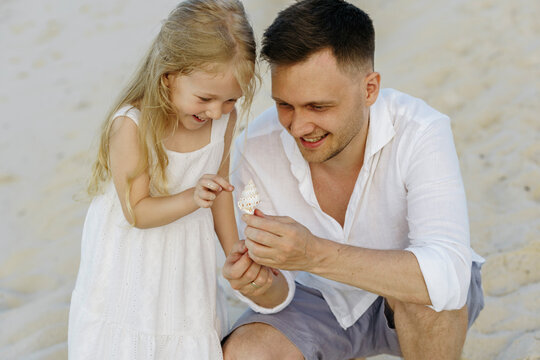 Happy father showing shell to daughter at beach