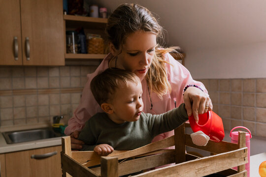 Mother and son watering seedlings in wooden crate at kitchen