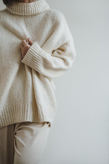 Closeup view of pretty young woman wearing warm knitted sweater pullover over white wall. Aesthetic...