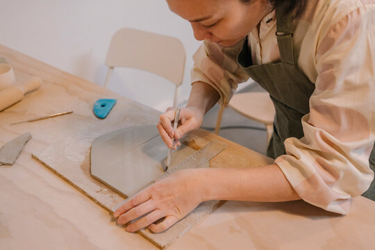 Skilled craftsperson cutting clay on table at pottery workplace