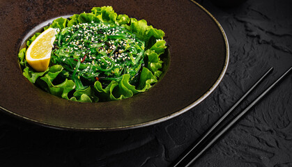 Fresh green seaweed salad with sesame seeds on dark plate
